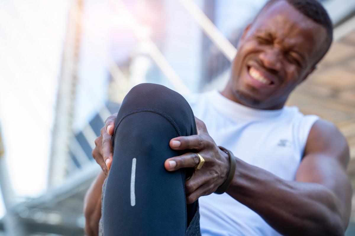 male runner bends over clutching his knee while in intense pain from an acute knee injury