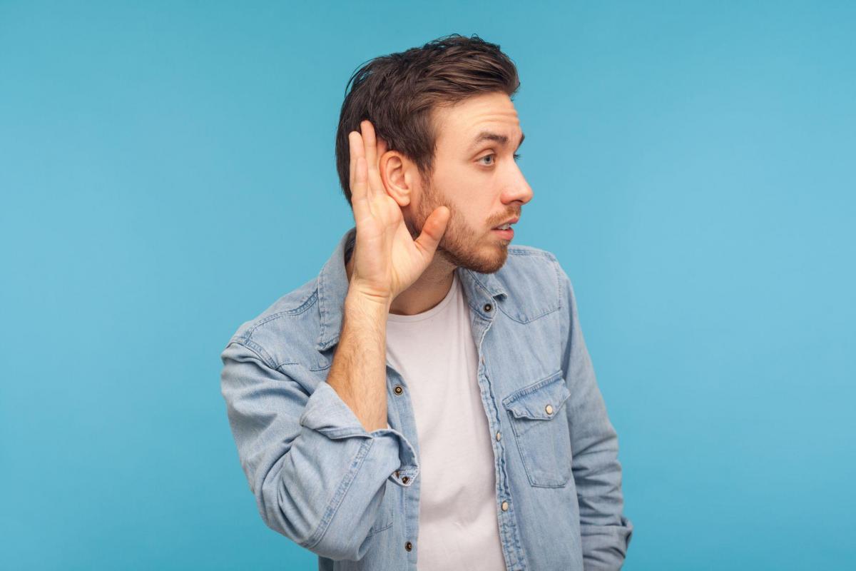 Man in worker denim shirt holding hand near ear and listening carefully