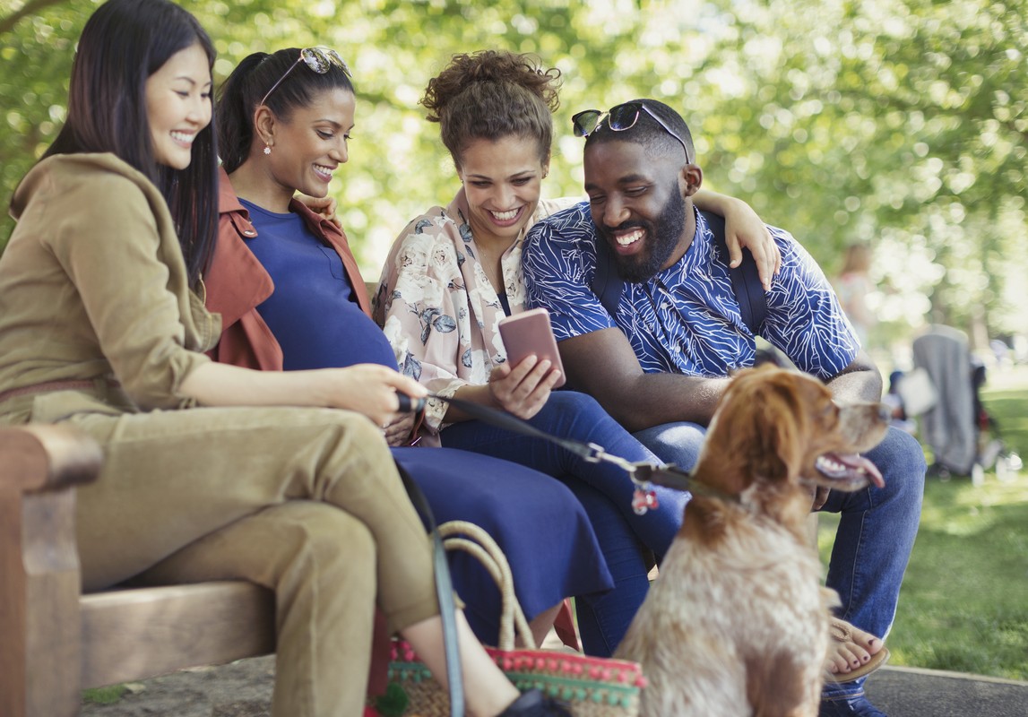 Pregnant woman and her friends using digital tablet on park bench