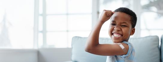 Child grinning while flexing with a bandage on his upper arm