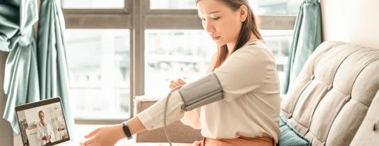 A person monitors their blood pressure during a virtual visit with a provider