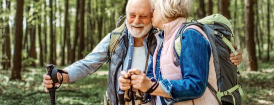 Active senior couple hiking with backpacks and trekking poles after successful hip replacement surgery, showcasing mobility and recovery outdoors.