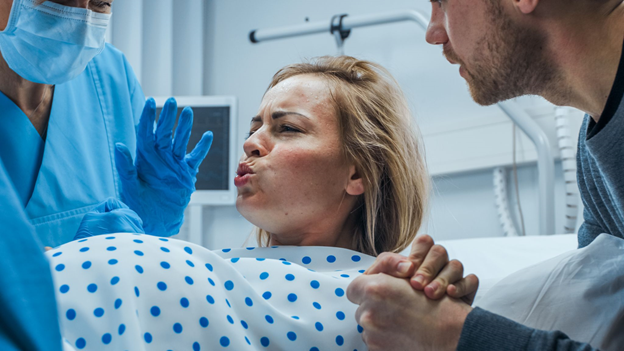 Woman in Labor Pushing Hard to Give Birth, Obstetricians Assisting, Spouse Holds Her Hand